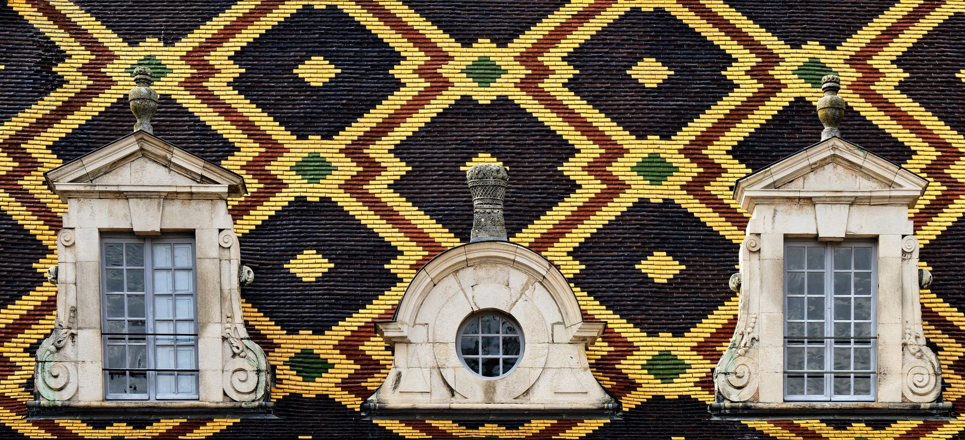 Toiture bourguignonne de tuiles vernissées à motifs géométriques et lucarnes en pierre