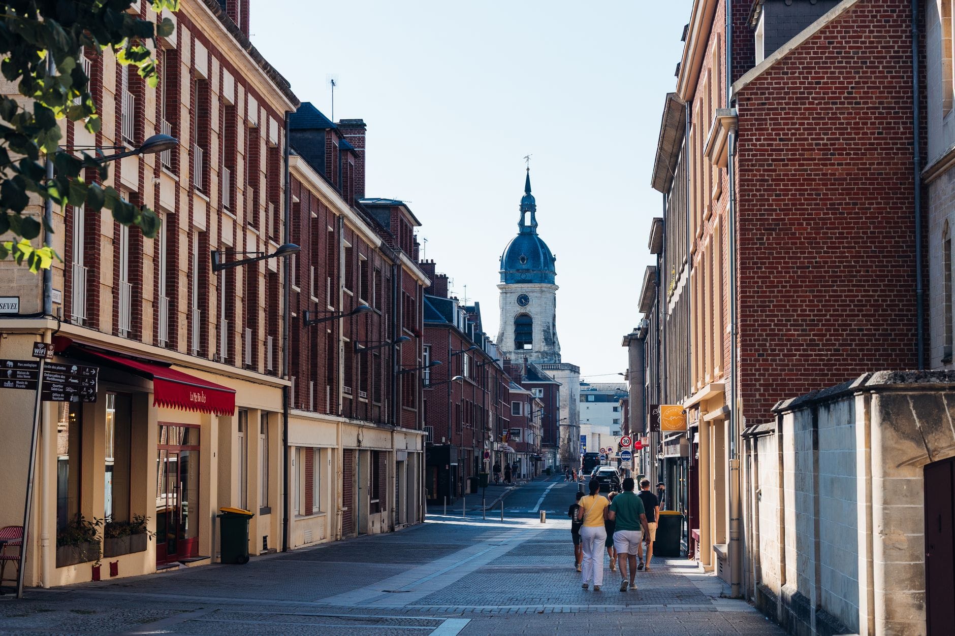 Rue bordée d'immeubles en brique rouge à Amiens, beffroi en arrière-plan